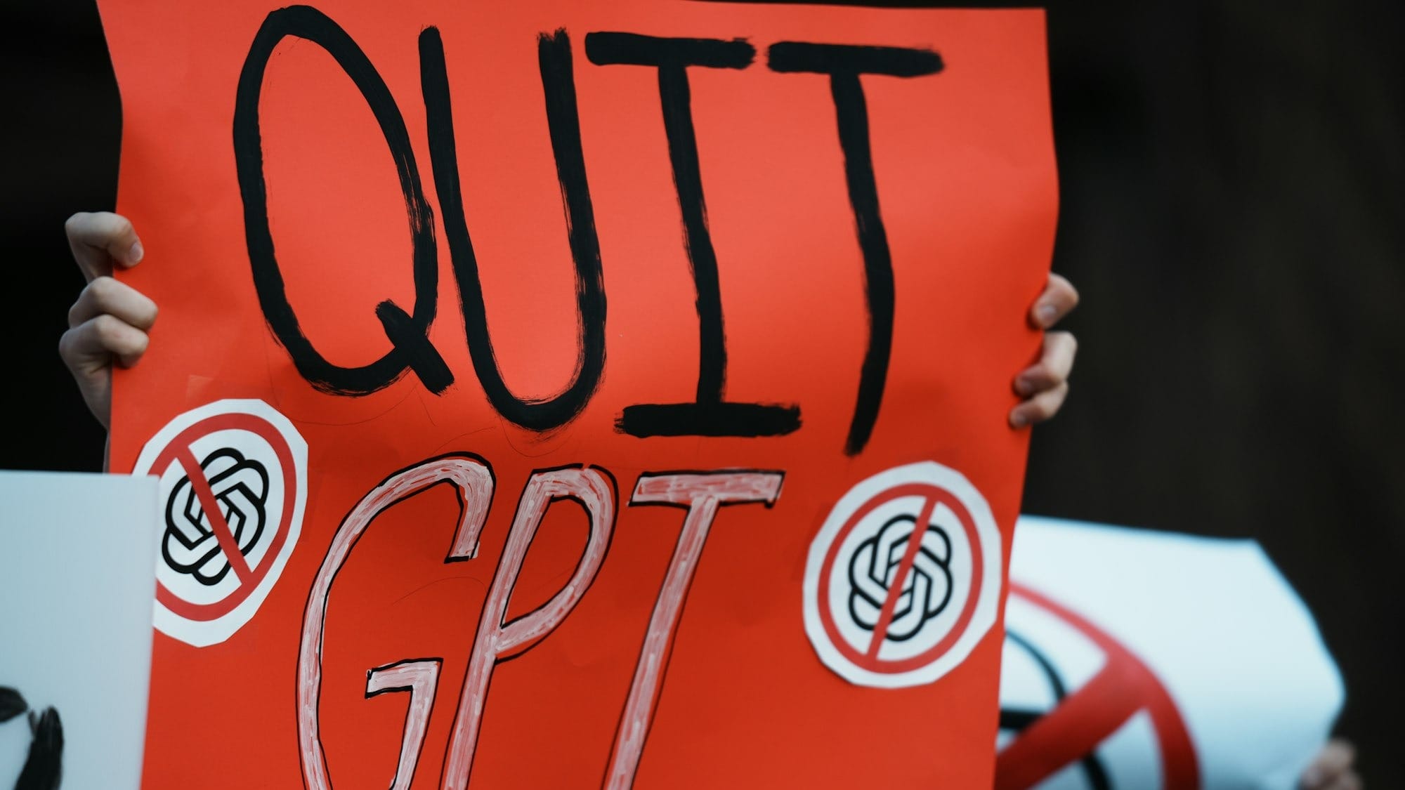 Protestors hold signs saying "quit gpt" with crossed-out logos.