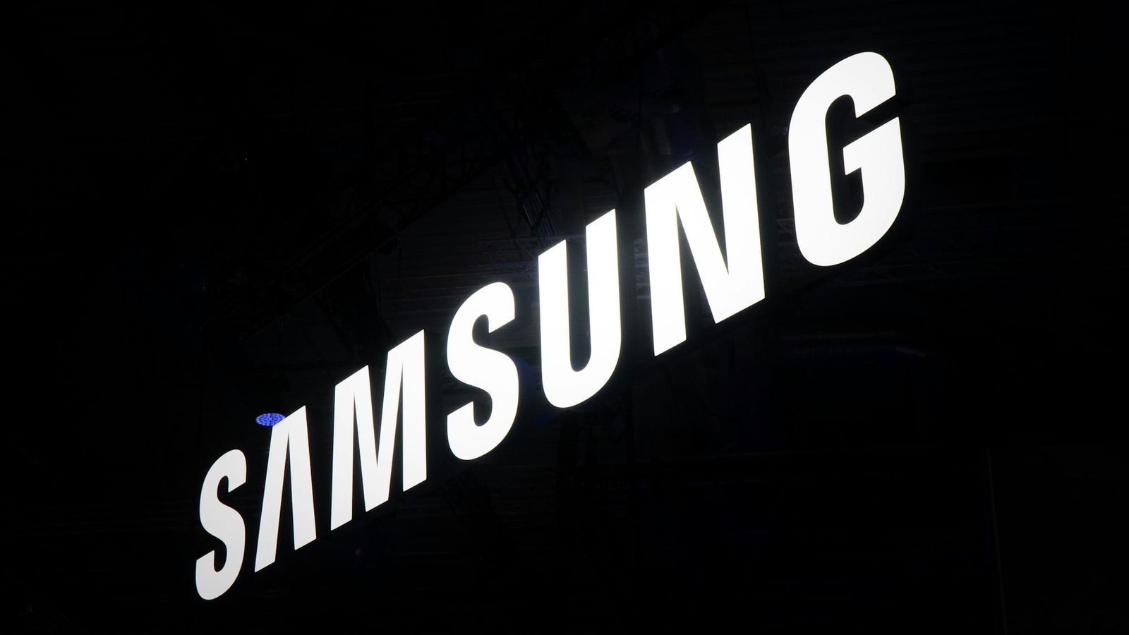 The image features the illuminated logo of Samsung, prominently displayed against a dark background. The logo is captured in a way that emphasizes its modern and sleek design.