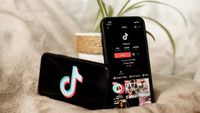 Two smartphones displaying the TikTok app are placed on a soft surface alongside a small potted plant. The phones show the app interface, highlighting user engagement and video content.