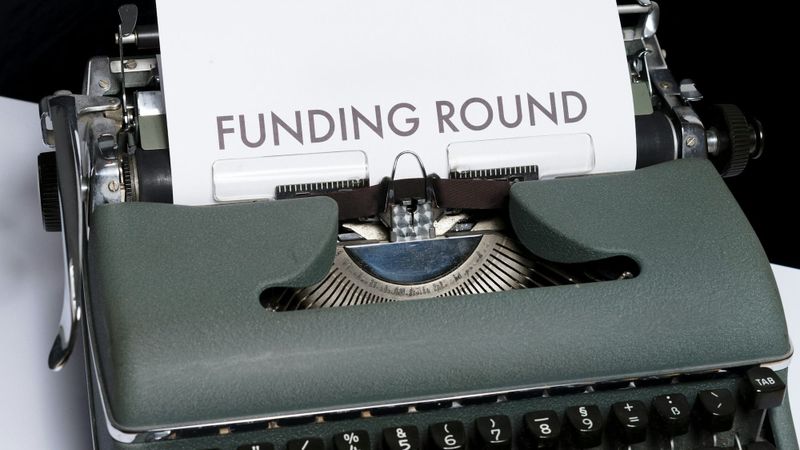 An antique typewriter with a sheet of paper emerging from it that reads 'FUNDING ROUND.' The image highlights the connection between traditional writing tools and modern financial concepts.