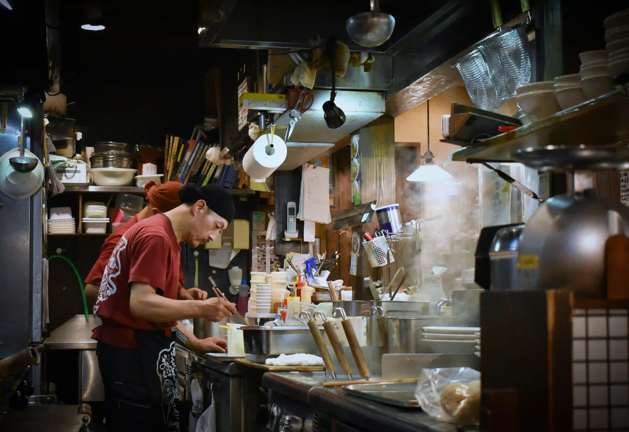 A dedicated Japanese chef working meticulously in a steamy, tightly packed, and authentic restaurant kitchen.