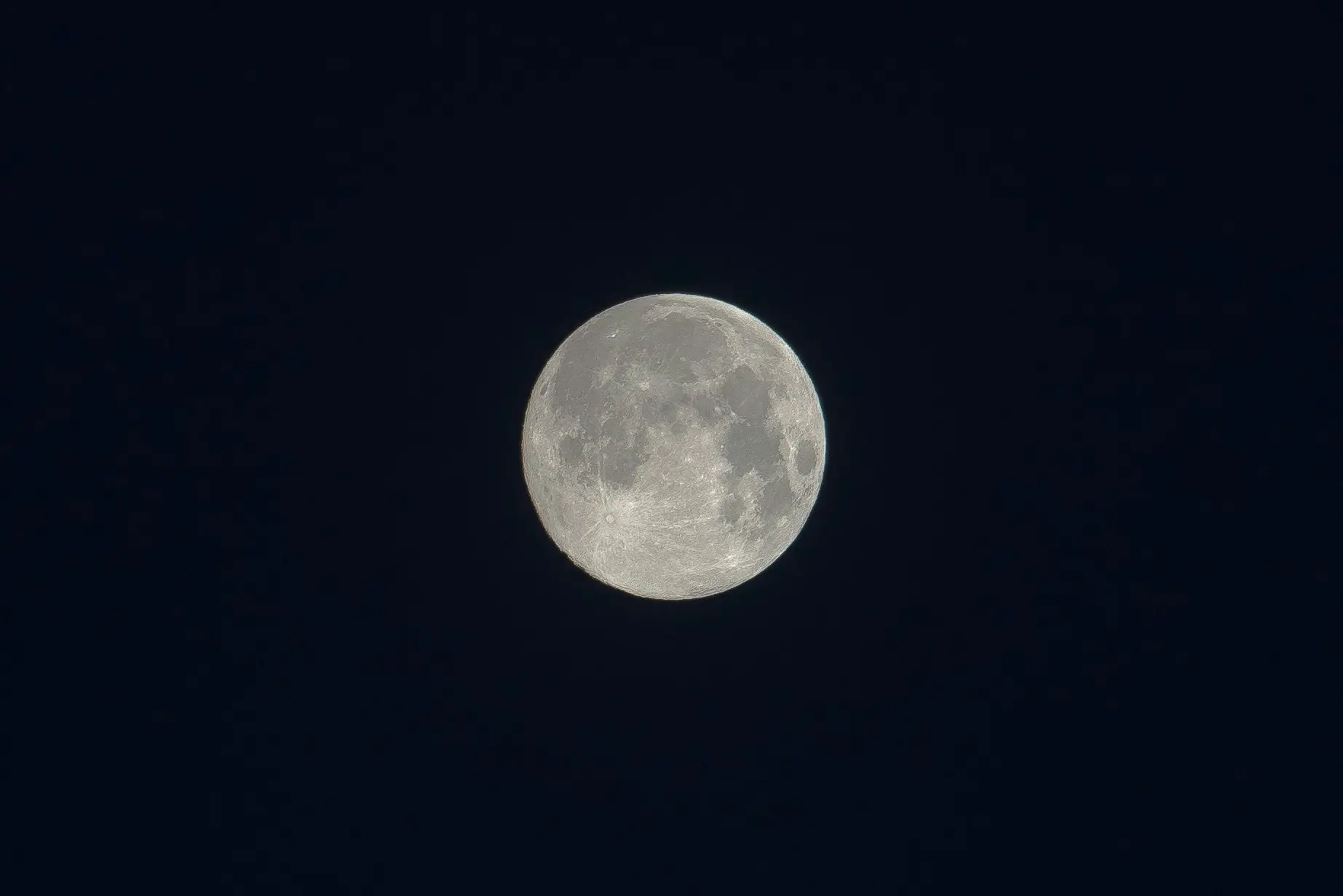 A highly detailed, pale full moon glowing against a pitch-black night sky, revealing its true color rather than a blue hue.