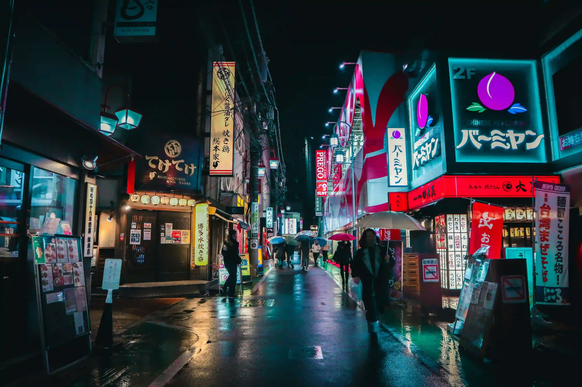 People walking with umbrellas on a wet, neon-lit street in Tokyo at night, reflecting vibrant city lights.