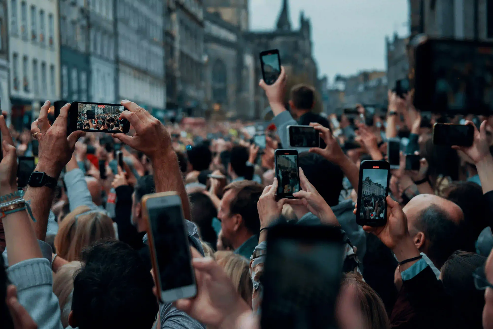 A dense crowd of tourists holding up smartphones to record, illustrating travel fatigue and the negative impact of algorithms on modern tourism.