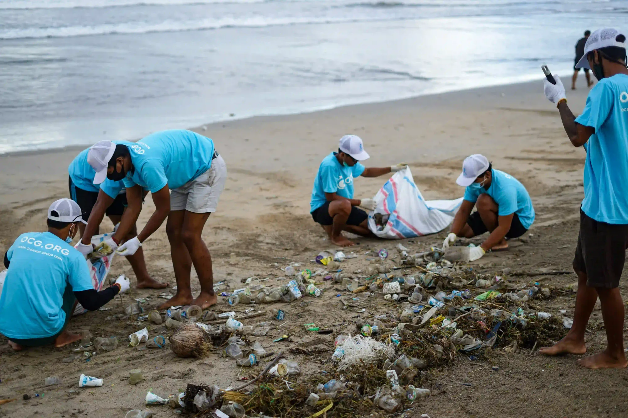 A group of volunteers cleaning up heavy plastic waste on a beach, representing the civic initiatives now caught in legal gray areas.