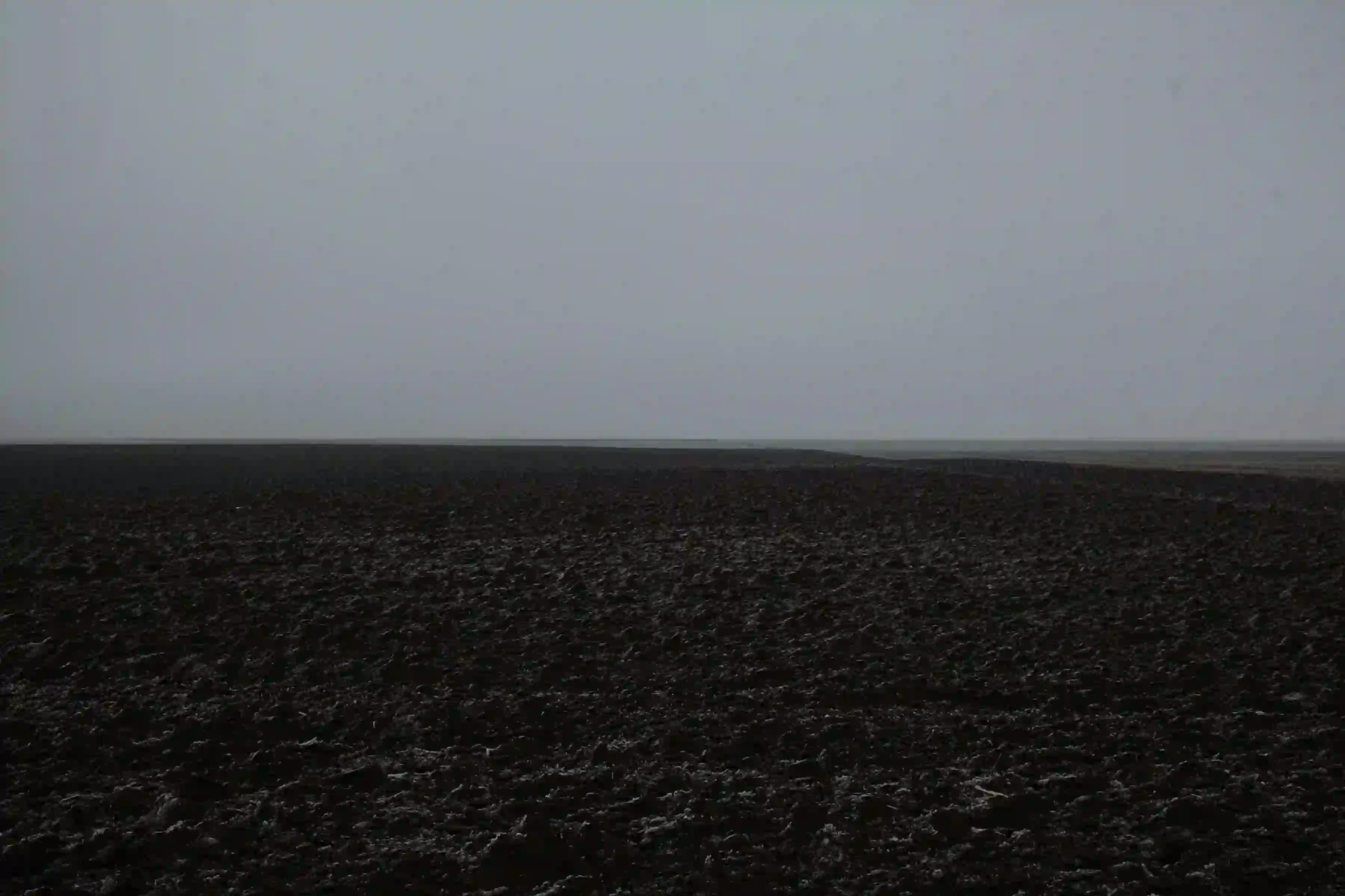 A vast, dark, and barren expanse of textured earth under a bleak grey sky, symbolizing the silent environmental devastation of landscapes like the Hunter Valley.