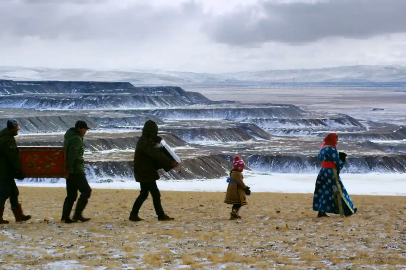 A stark contrast in the documentary Behemoth, showing local people in traditional clothing walking against the backdrop of a massive, devastated open-pit coal mine in Inner Mongolia.
