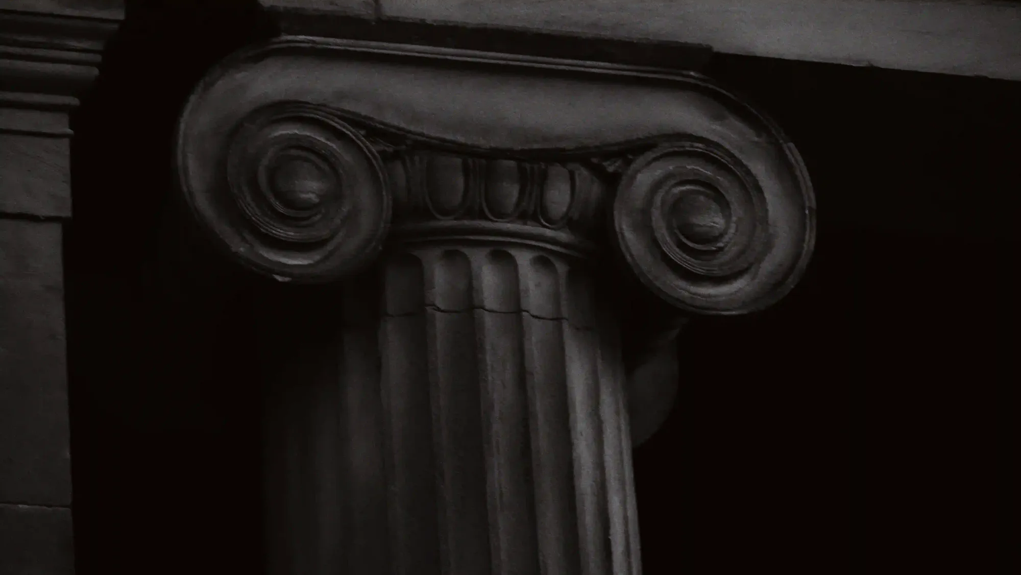 A dark, moody close-up of a classical carved stone column, highlighting the heavy and uncompromising nature of marble.