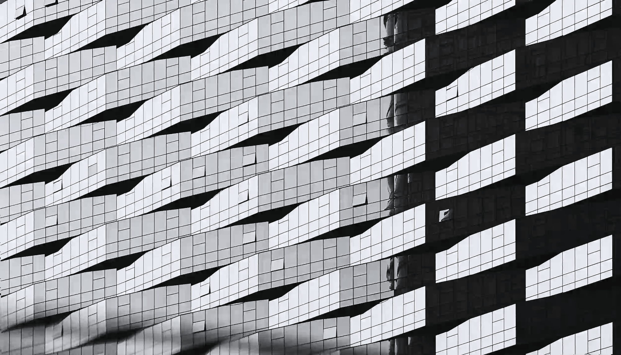 Abstract black and white view of a repetitive glass corporate building facade, representing industrial scale and corporate deflection.