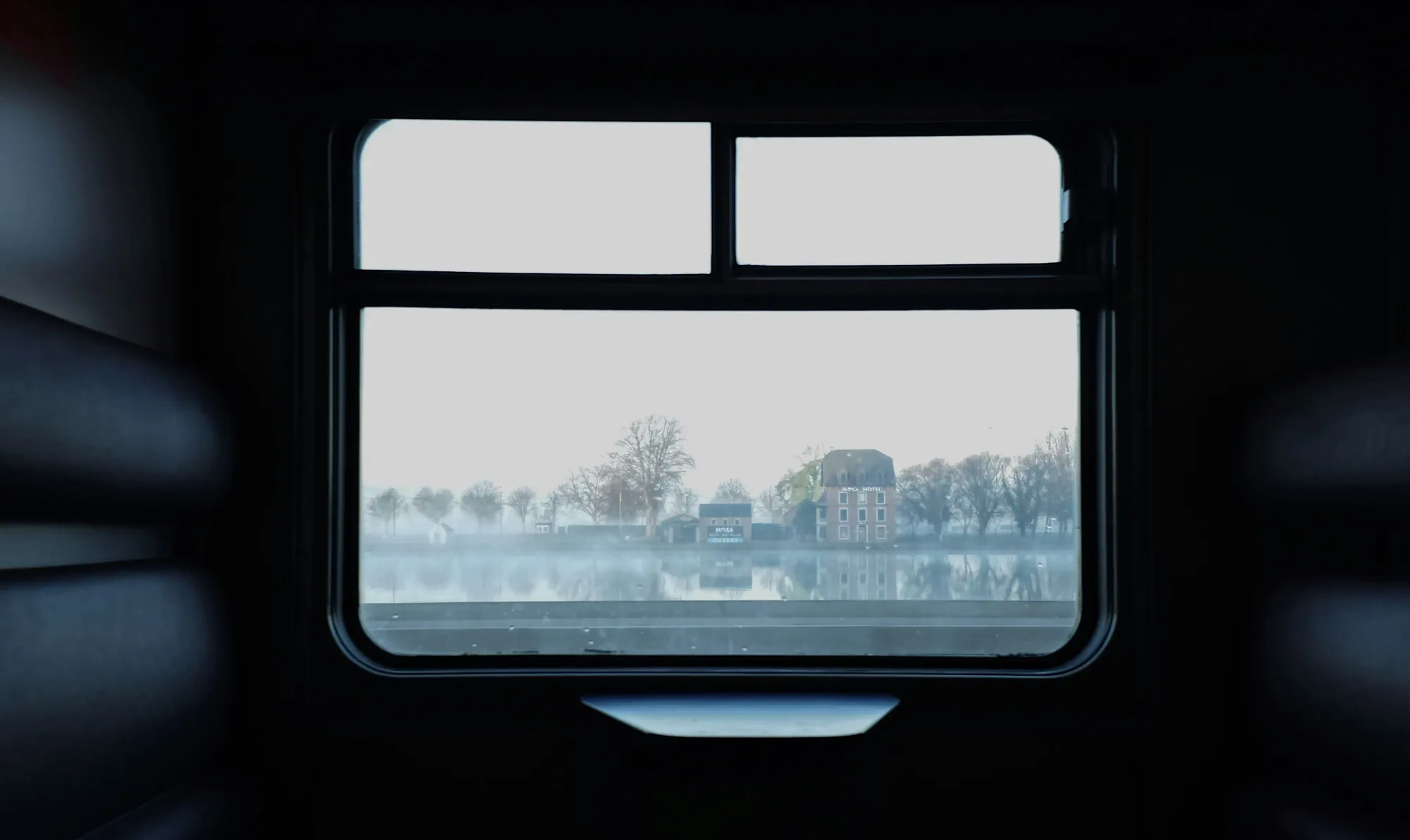 A cinematic, moody view from a dark train window overlooking a misty landscape, representing the mystery travel trend and the death of the itinerary.