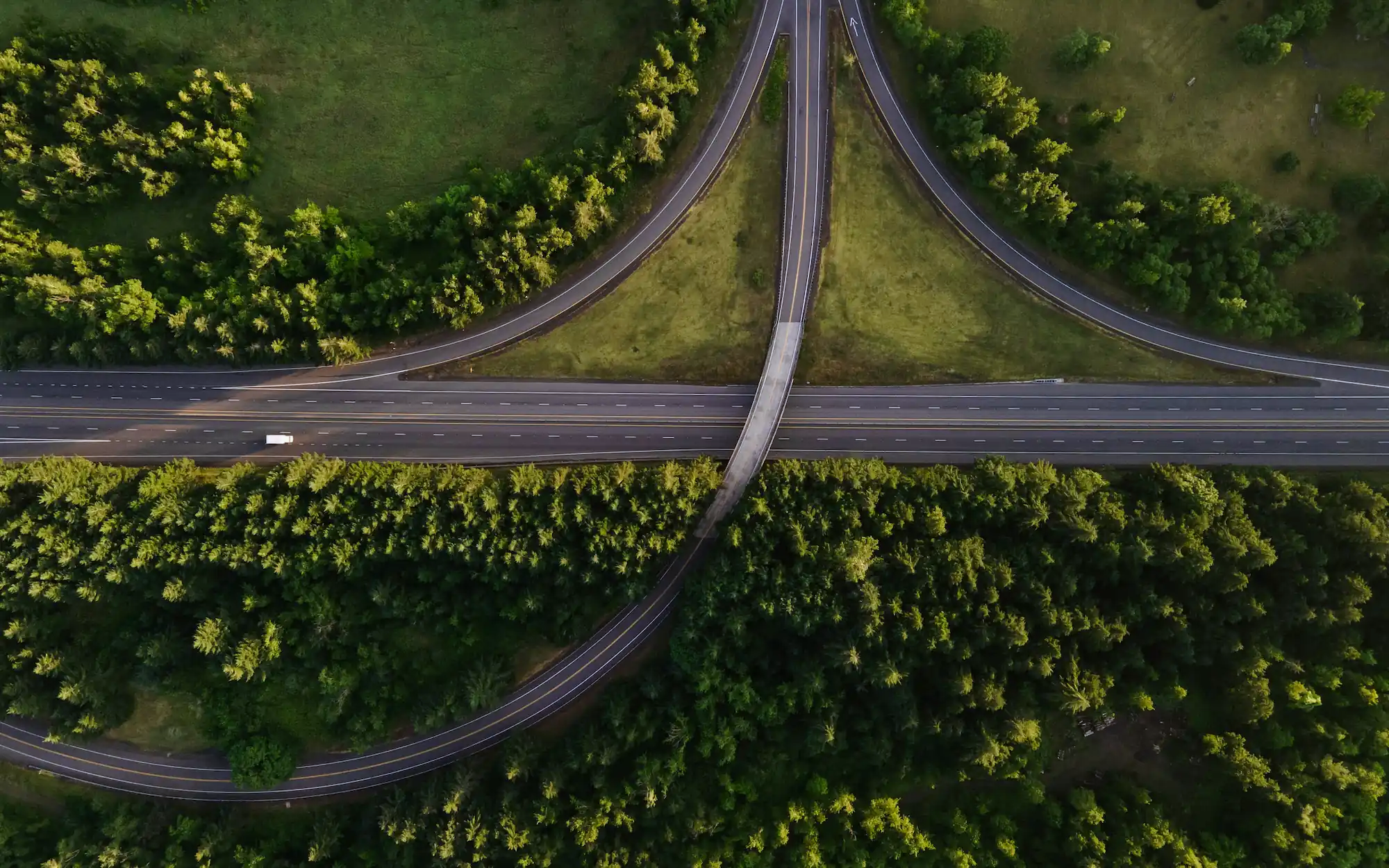 Aerial view of an almost empty highway intersection surrounded by trees, visualizing the concept of systemic slack and necessary empty space in traffic flow.