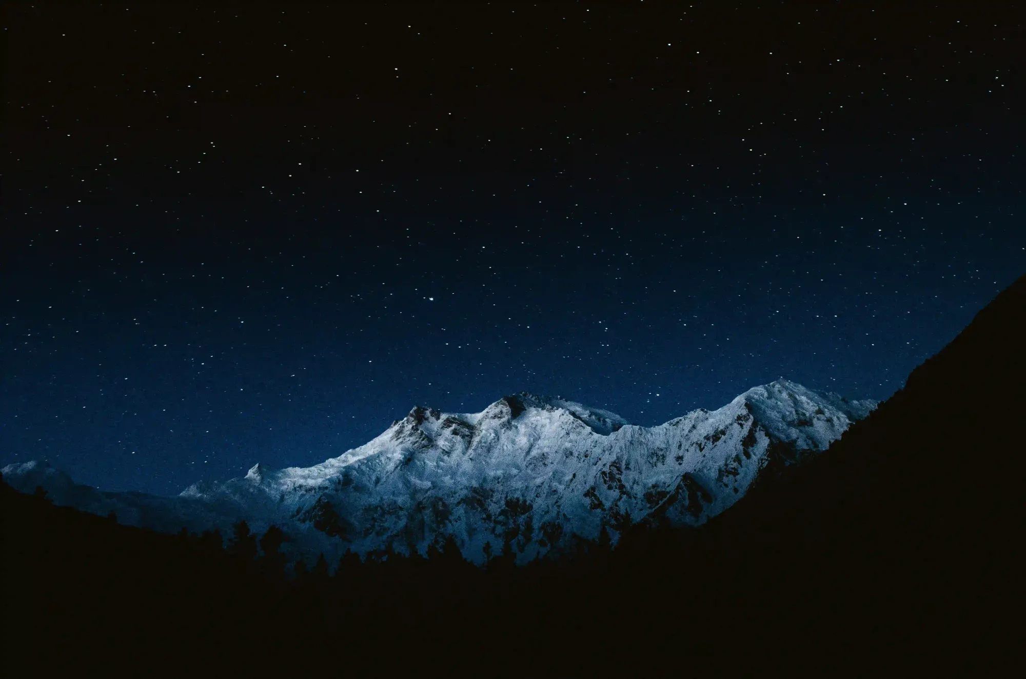 A stark, starry night sky over a massive snow-capped mountain peak, emphasizing the silent scale of the universe.