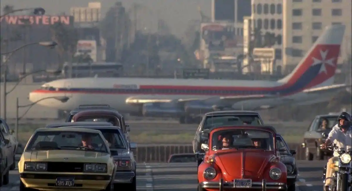 A chaotic urban scene from the documentary Koyaanisqatsi, featuring heavy highway traffic with a massive commercial airplane in the background, symbolizing modern human frenzy.