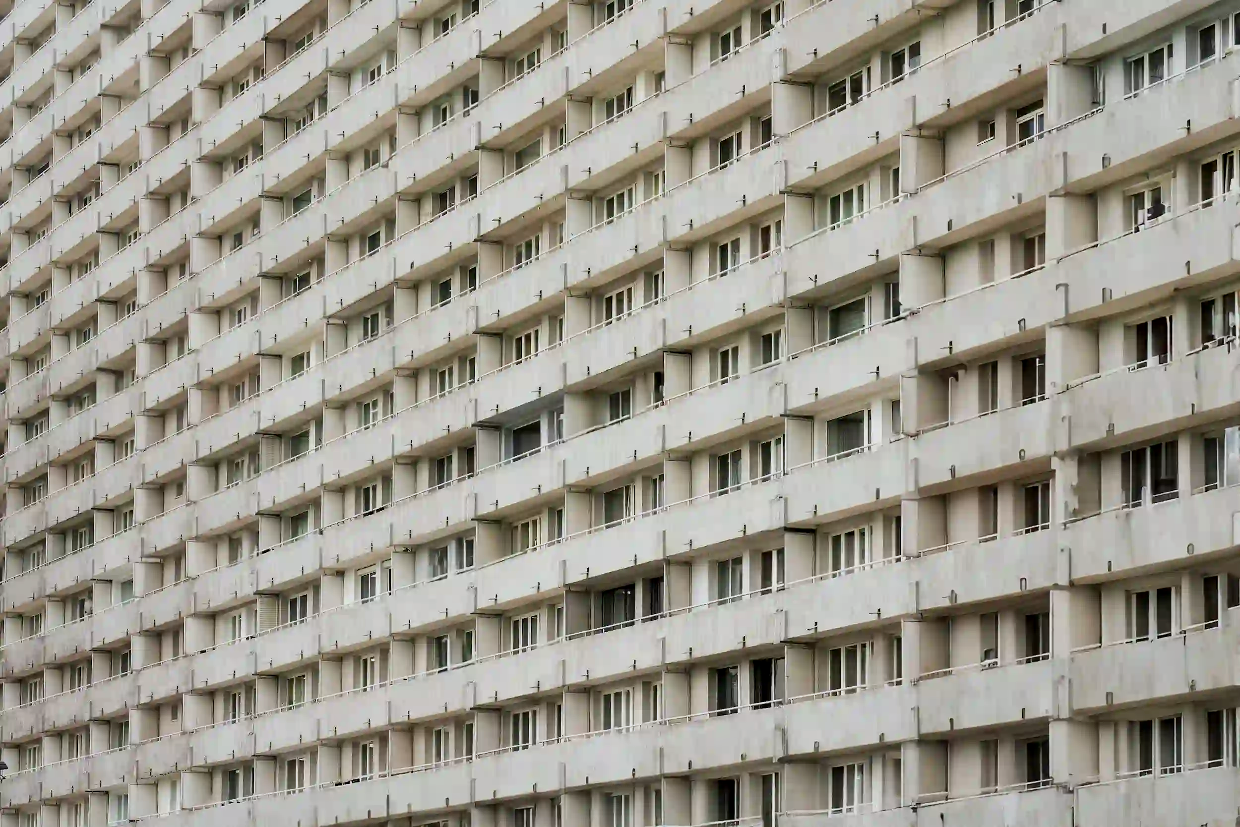 A massive, repetitive facade of a gray concrete building, illustrating the sterile and soulless nature of modern urban development and the loss of architectural memory.