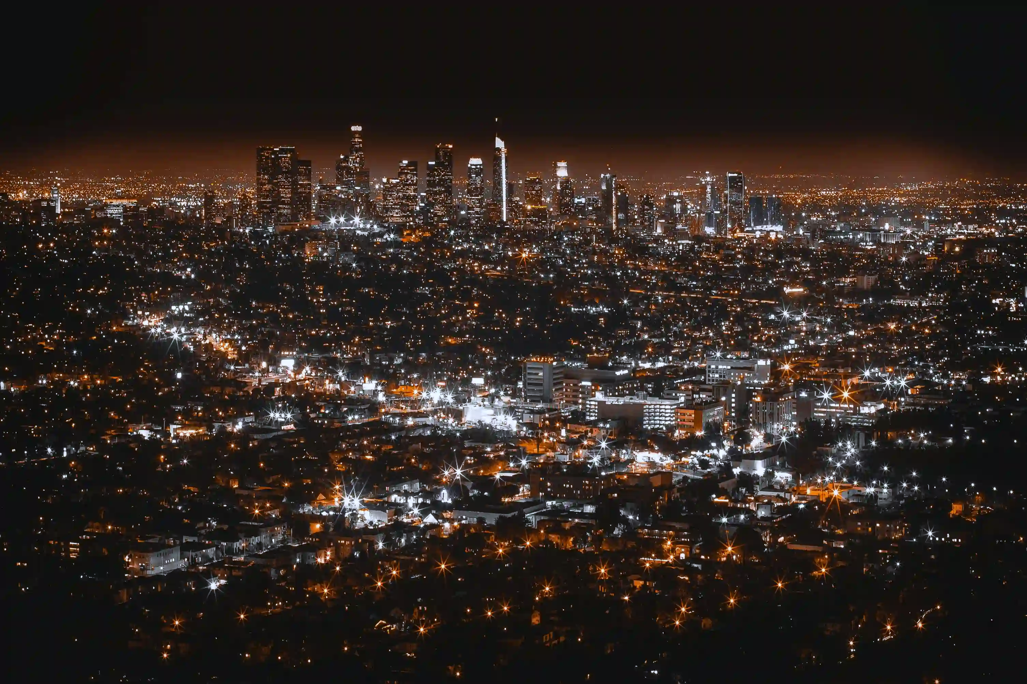 Aerial night view of a sprawling city skyline, illustrating the orange haze of synthetic twilight caused by extreme urban light pollution.