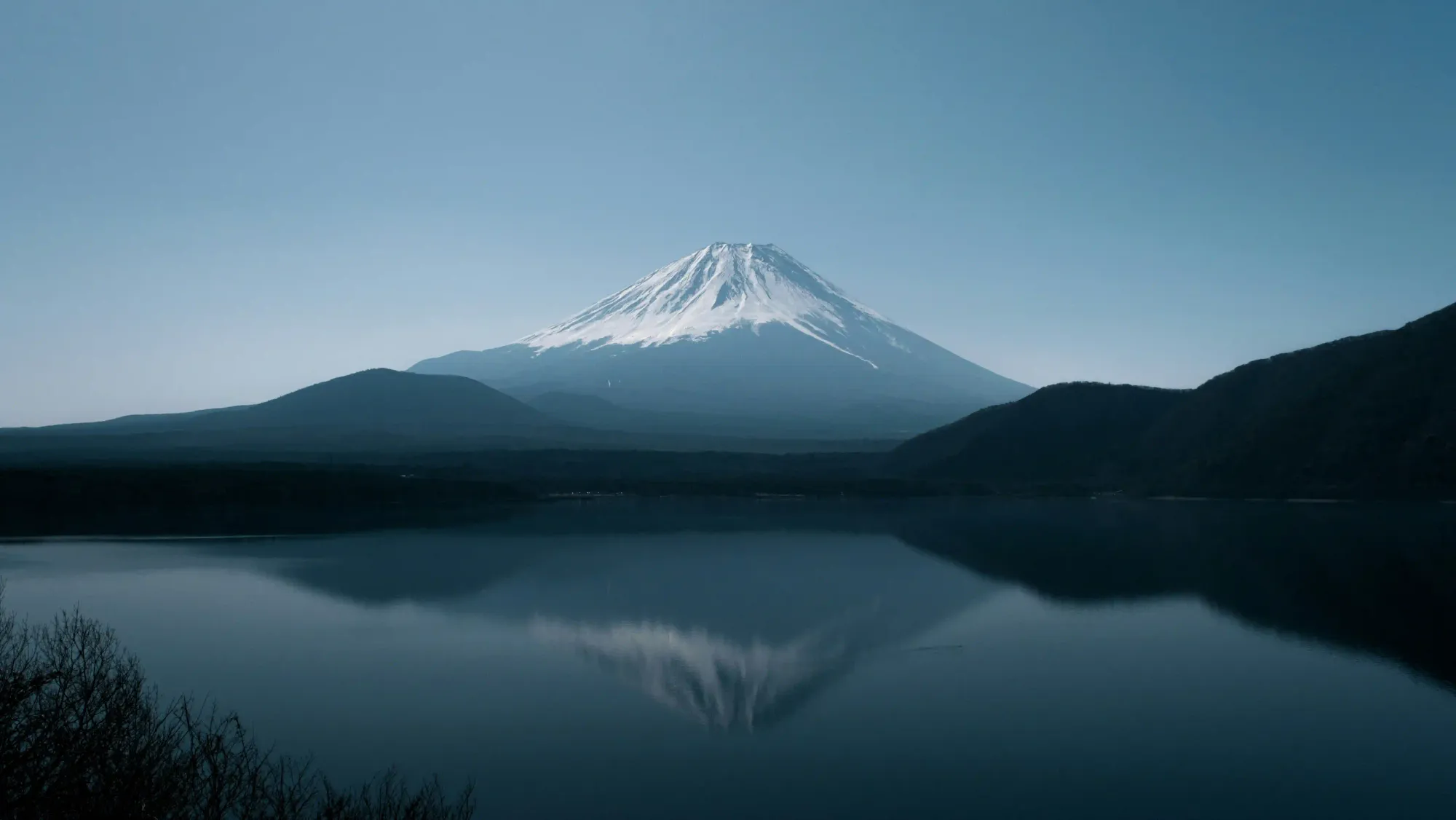 A serene and minimalistic morning view of Mount Fuji reflecting on the calm, blue waters of Lake Motosu in Japan.