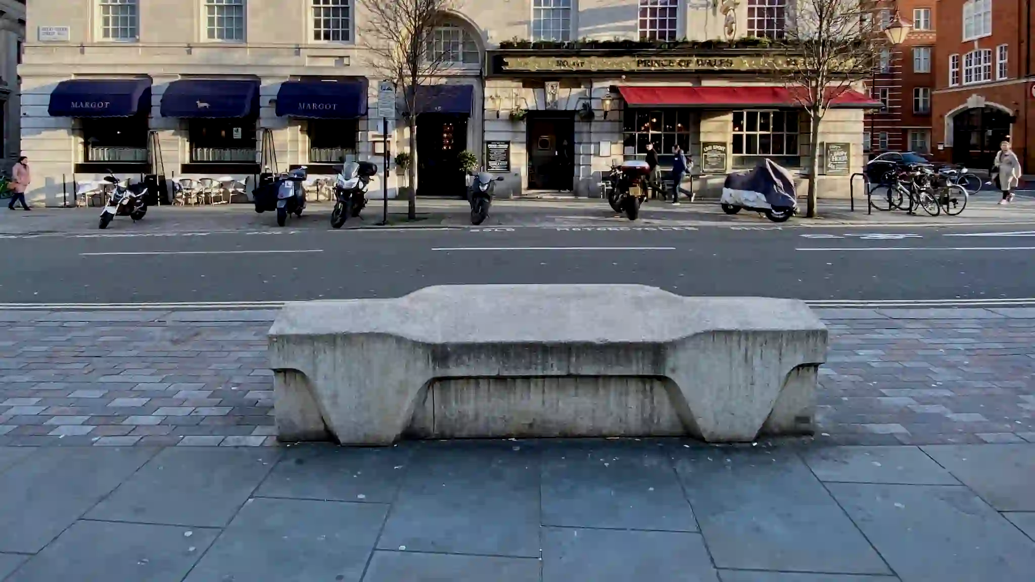 A solid grey concrete Camden Bench on a London street, an example of hostile architecture designed to prevent sleeping and skateboarding.