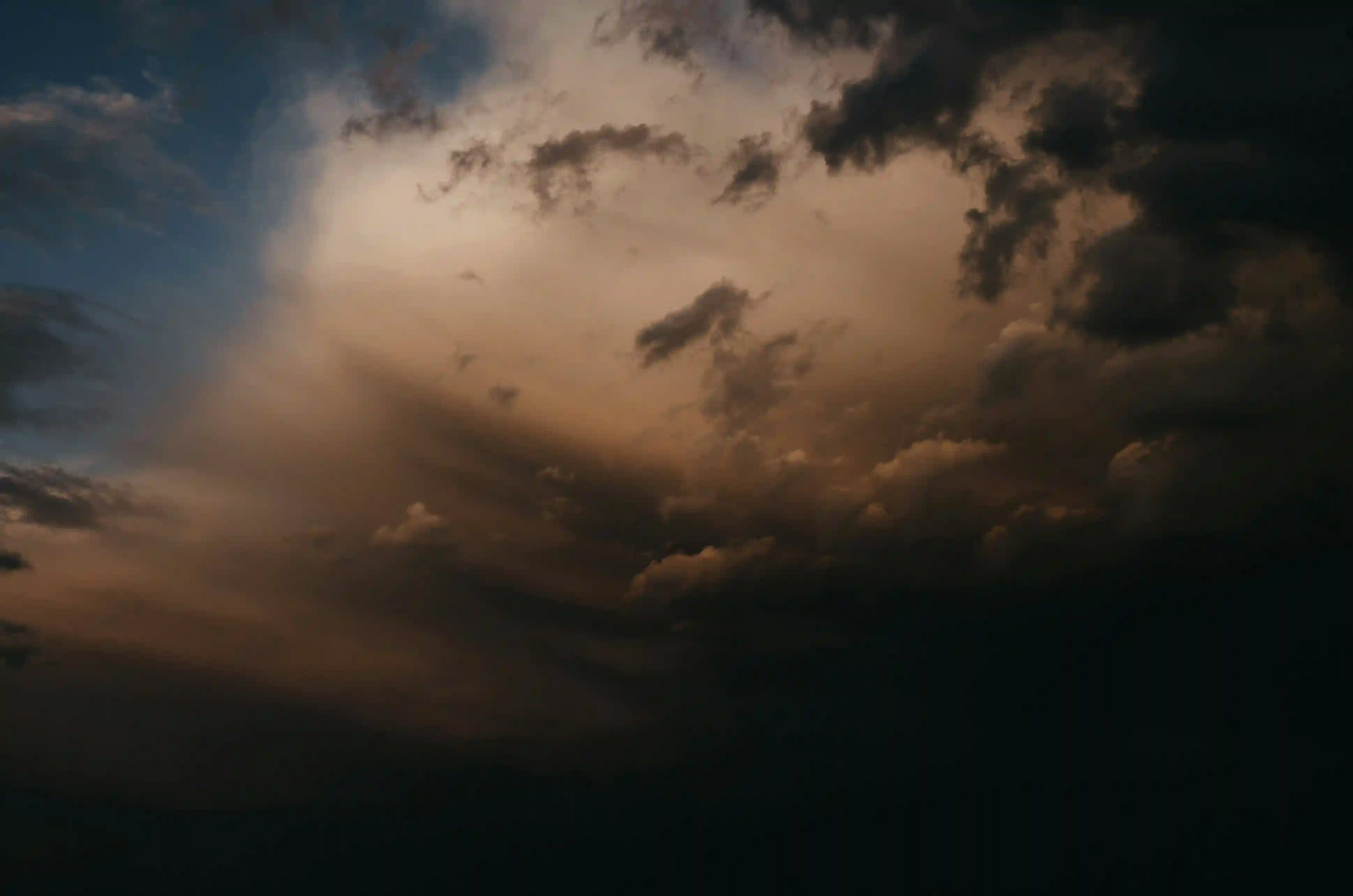 Heavy, dark storm clouds partially illuminated from behind by a dim, warm orange sunlight.