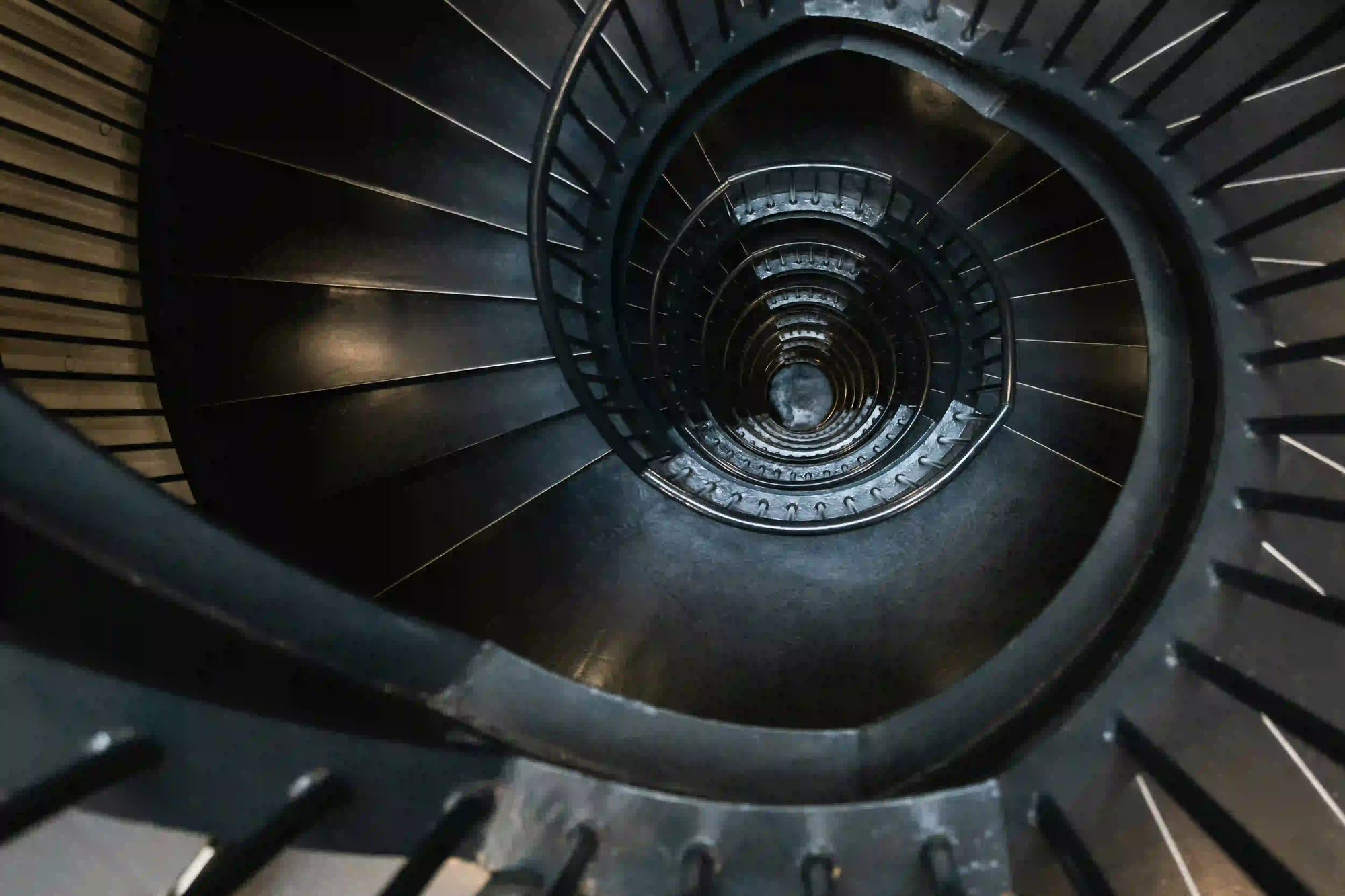 A top-down view looking into the deep, dark void of an industrial spiral staircase, representing the psychological echo of architectural spaces.