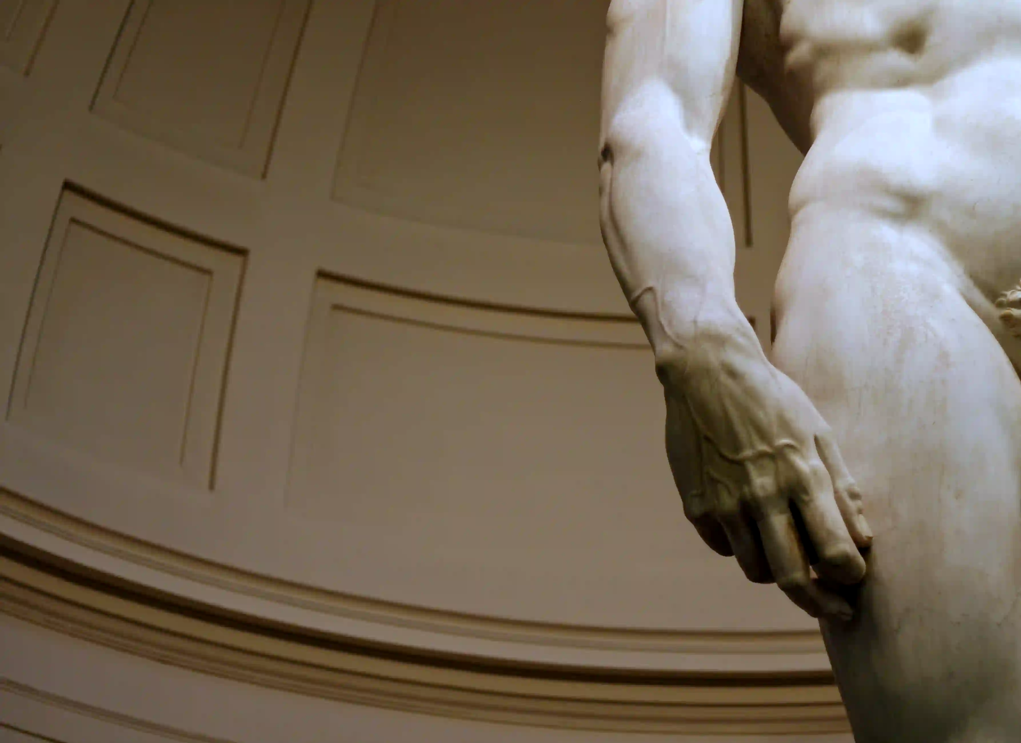 A close-up of a classical marble statue's hand and torso, highlighting the intimidating anatomical details, veins, and monumental scale of Renaissance art.