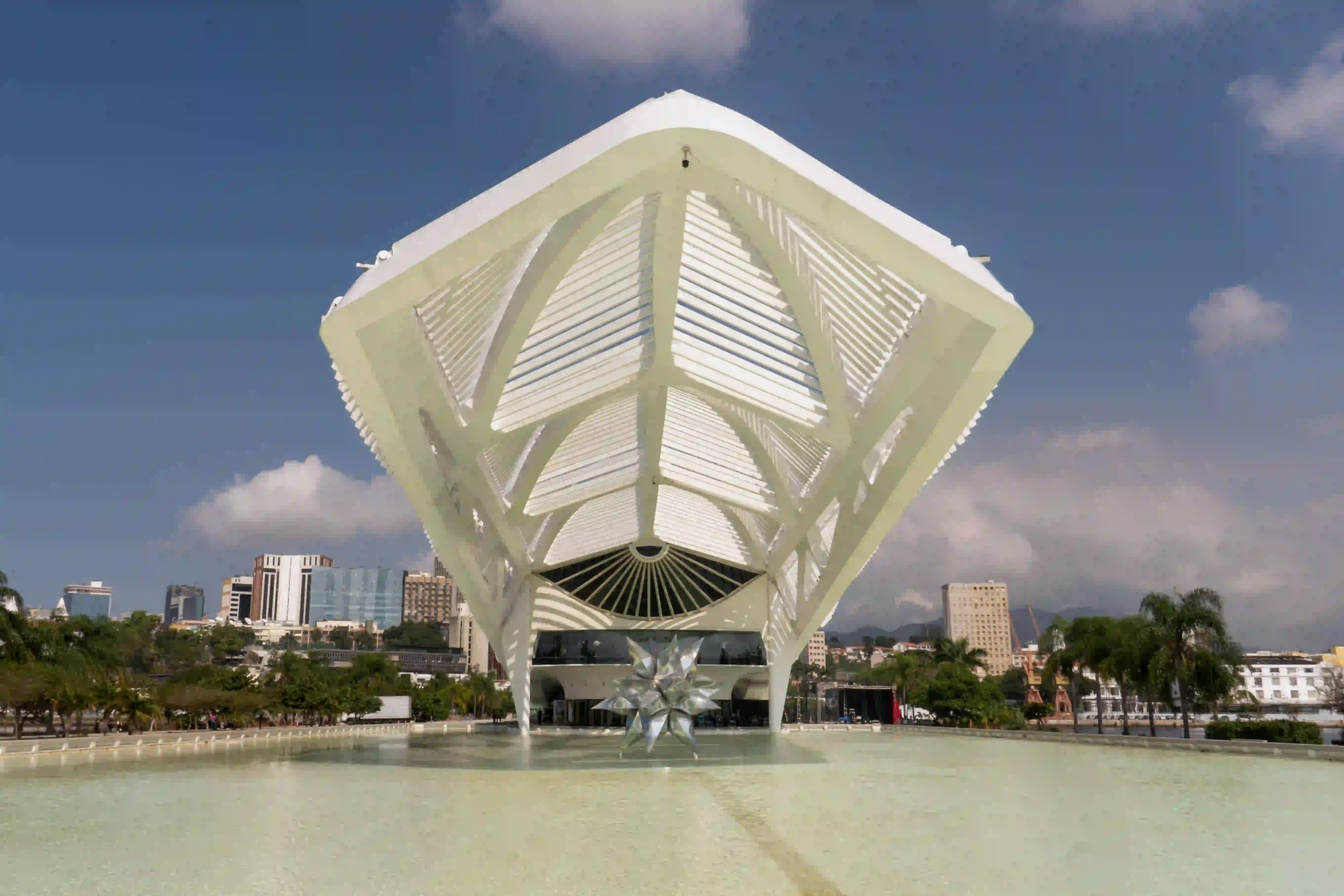 The skeletal, futuristic white structure of the Museum of Tomorrow extending over a reflecting pool in Rio de Janeiro.