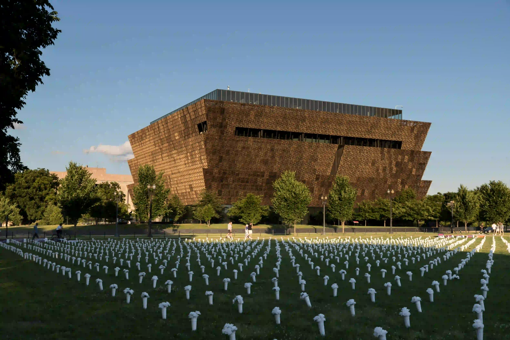 The bronze, three-tiered corona exterior of the National Museum of African American History and Culture in Washington D.C., with a solemn memorial of white markers on the lawn in the foreground.