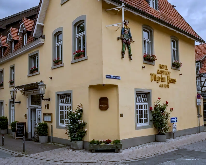 The corner exterior of Pilgrimhaus, a historic yellow building in Soest, Germany, featuring traditional signage and a sculpted figure on its facade.