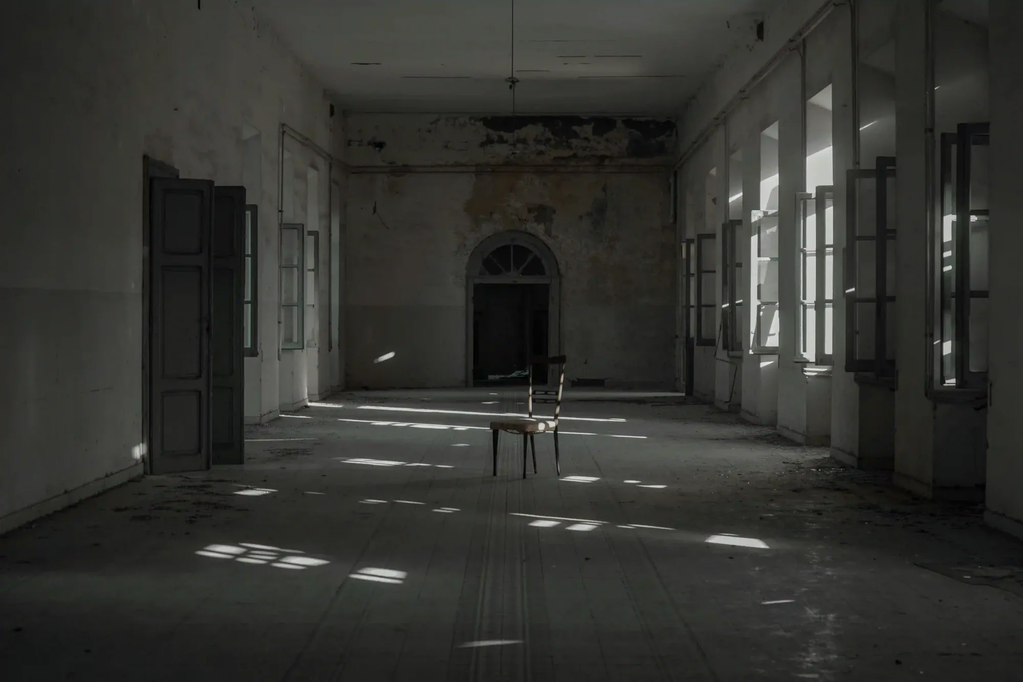 A solitary wooden chair in a vast, abandoned room with natural light casting long shadows, symbolizing ecological grief and absence.