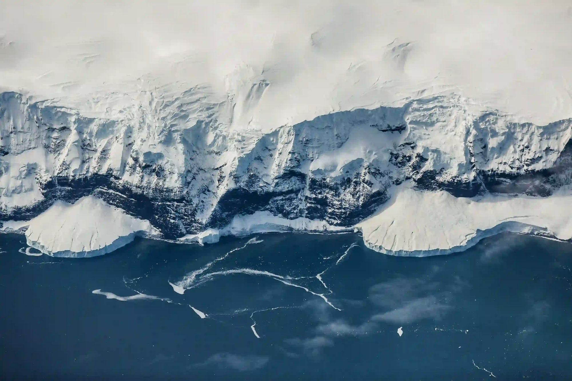 An aerial view of massive, textured ice cliffs meeting a deep blue ocean, resembling a remote map or model.