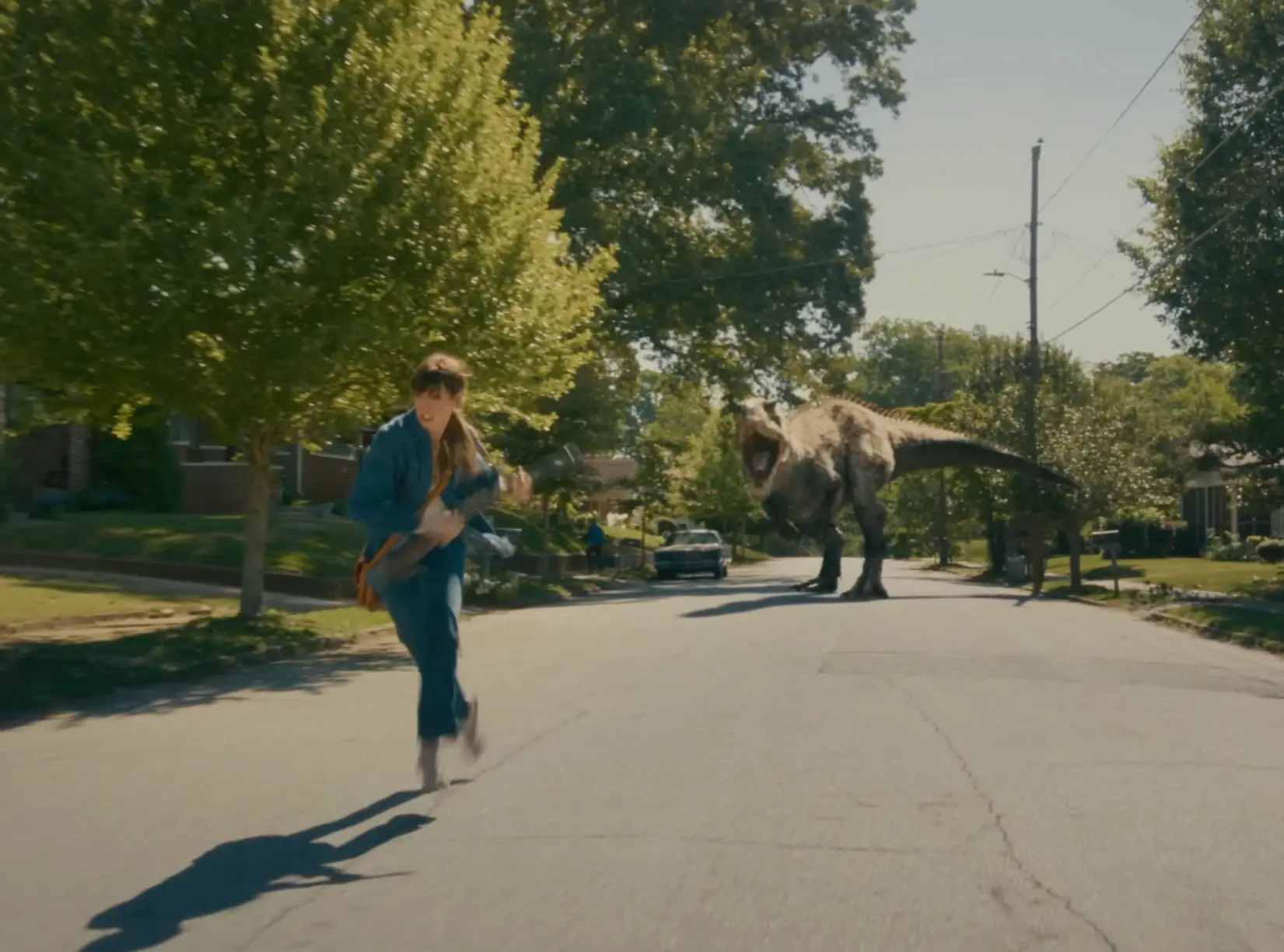 A woman running frantically down a suburban street as a massive T-Rex chases her, illustrating immediate physical danger.