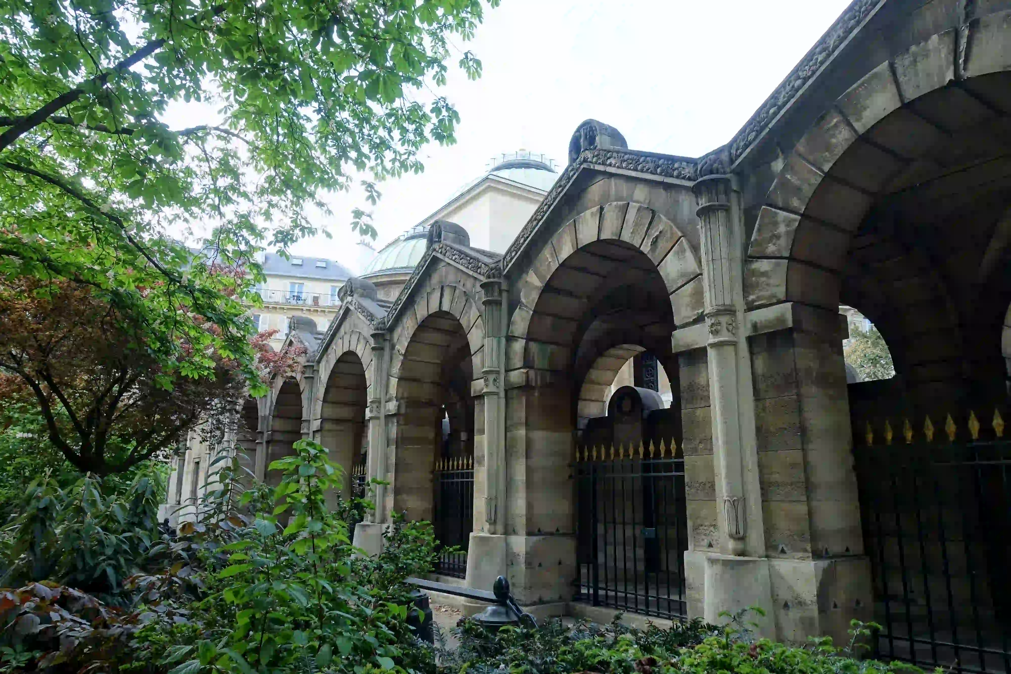 Heavy neoclassical stone arches and thick pillars of the Chapelle Expiatoire in Paris, standing as an architectural barrier against the city noise.