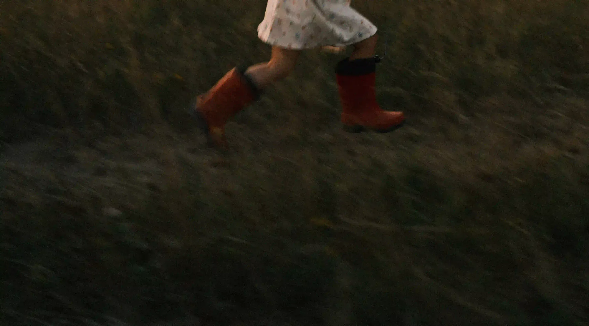 A low-light, motion-blurred shot of a child in red boots running through a dark grassy field, symbolizing hope as a forward action.