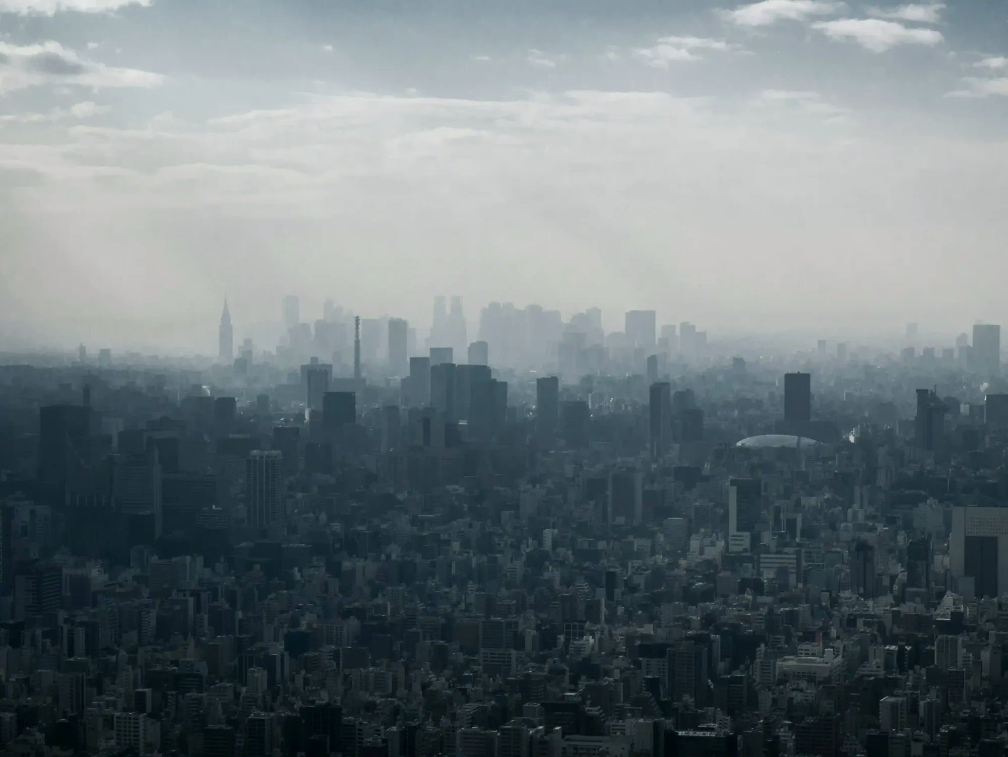 A dense, foggy, and desaturated view of a metropolitan city skyline, conveying a sense of claustrophobic concrete and urban isolation.