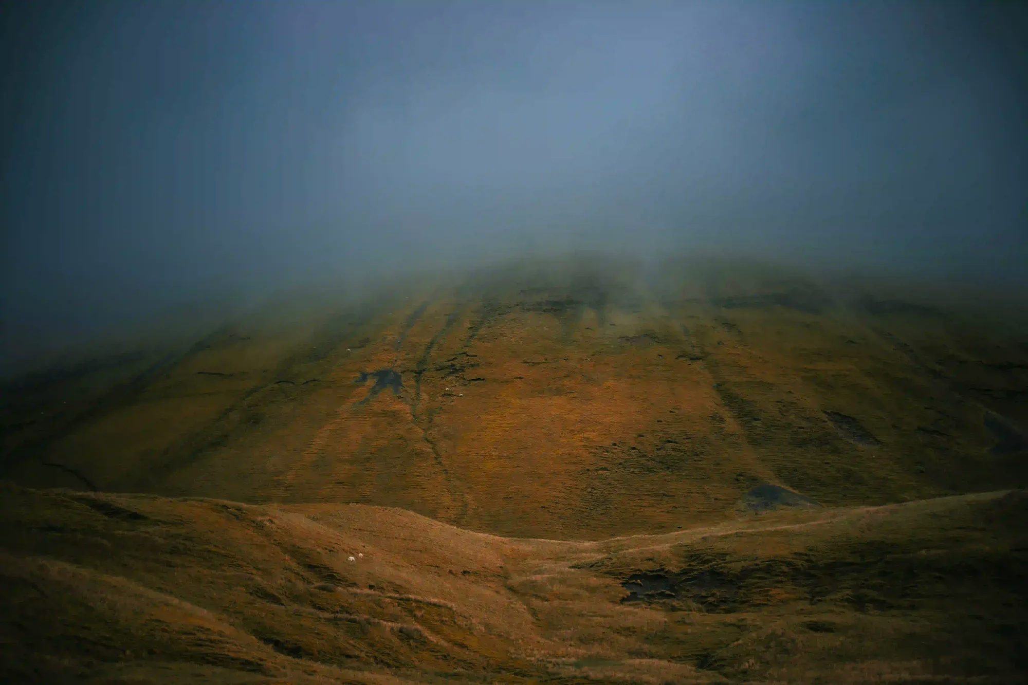 Moody, low-exposure view of a heavy green mountain mass fading into dense fog, representing the physical weight of the Earth.