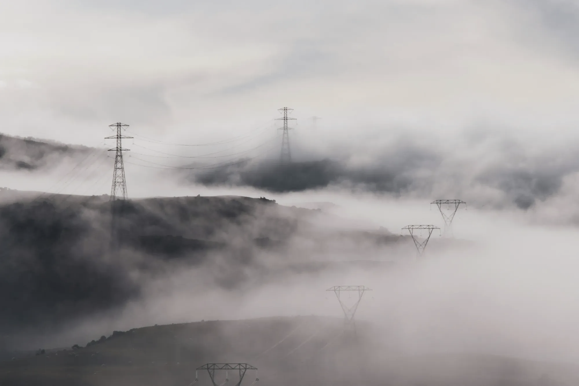 High-voltage power line towers fading into dense, rolling fog, symbolizing invisible electromagnetic fields and navigation networks.