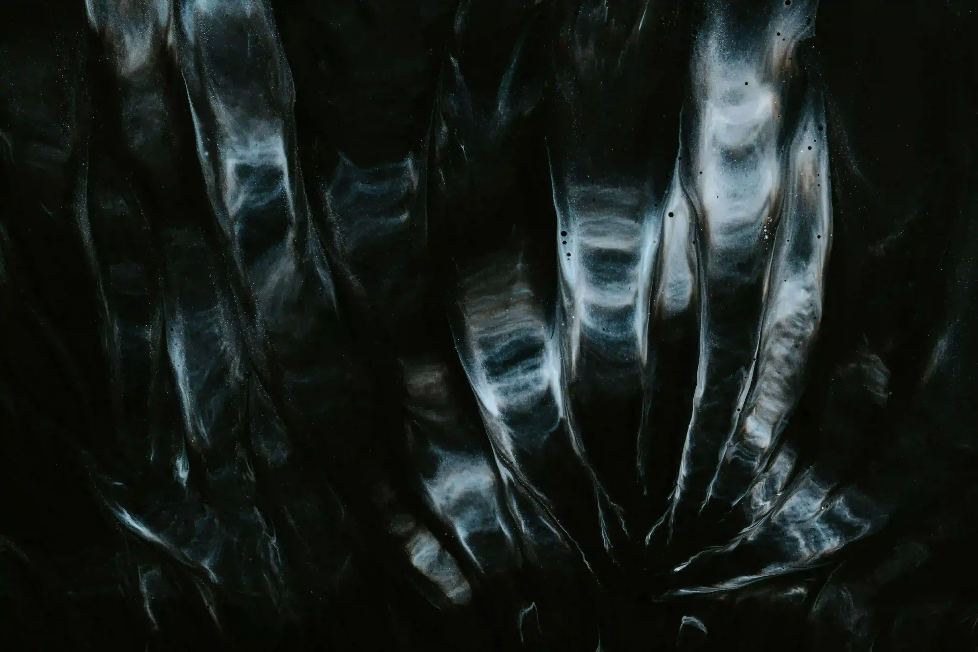 A dark, abstract texture of swirling light and deep shadows, resembling a distorted glass lens or cosmic matter.
