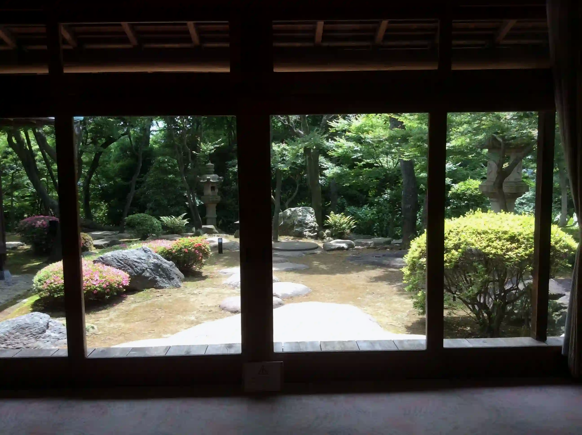 Looking from a dark traditional wooden room through sliding door frames into a brightly lit, serene Japanese garden at Kyu-Asakura House.