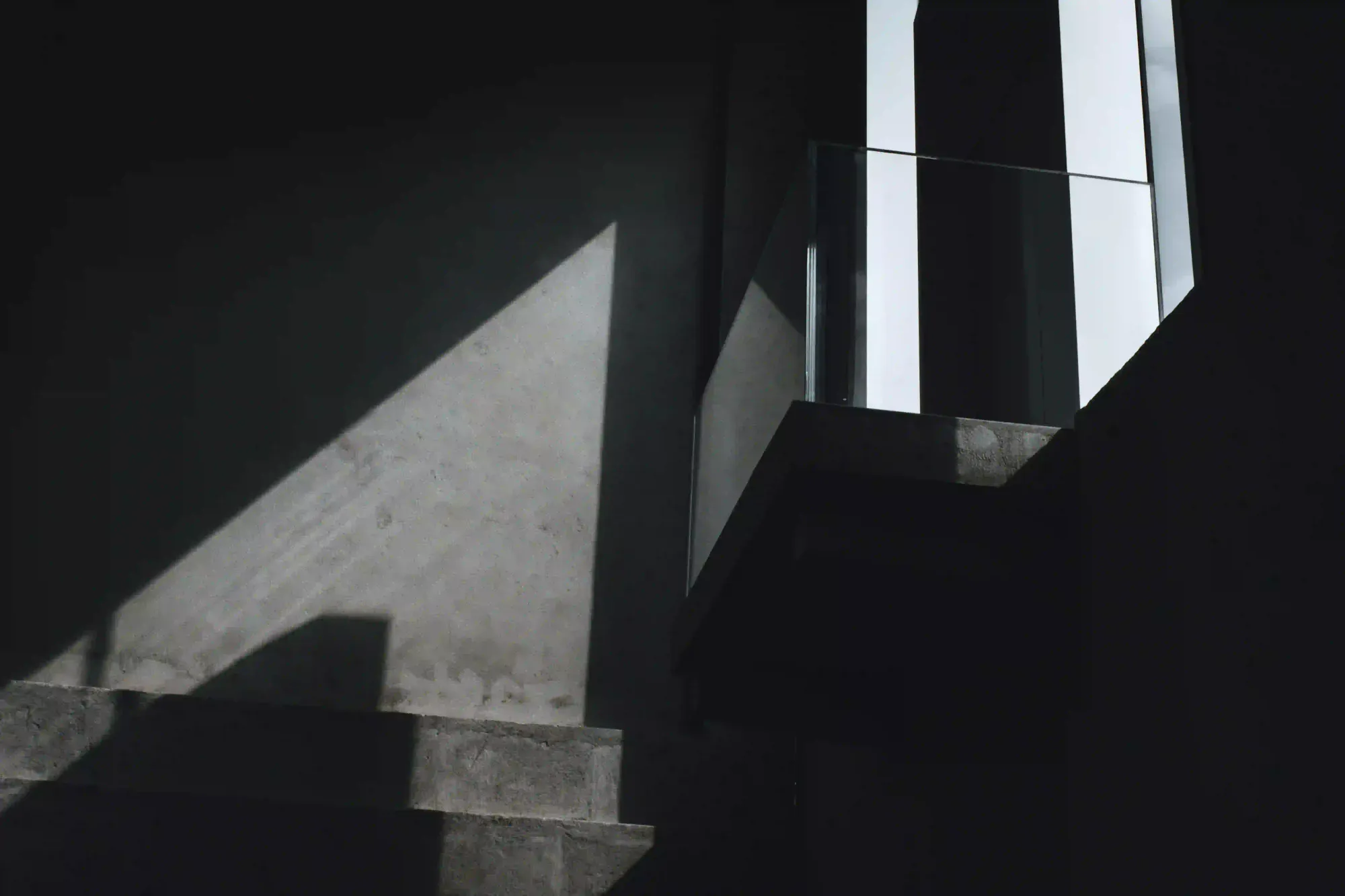 Abstract geometric shadows cast on a raw concrete wall by a sharp beam of natural light in a minimalist architectural space.