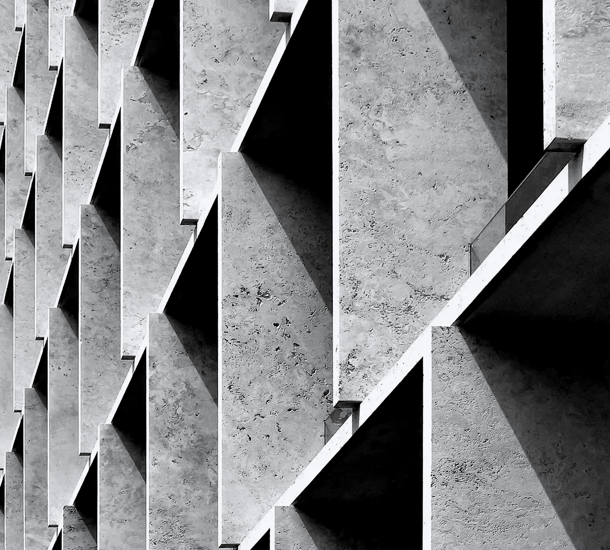 Black and white architectural detail of a concrete building with sharp, overlapping geometric ledges casting deep shadows.