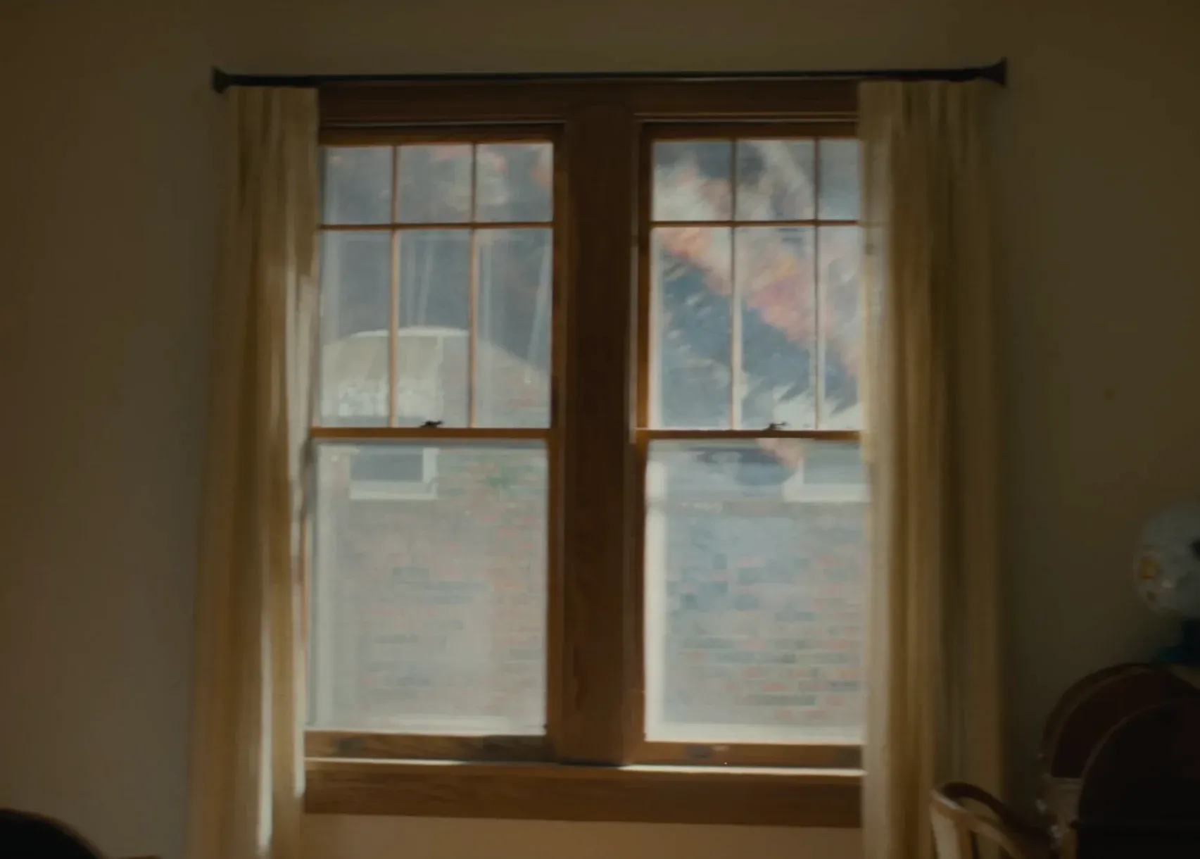 A dimly lit, quiet room looking out a window, representing the psychological isolation of modern suburban life.