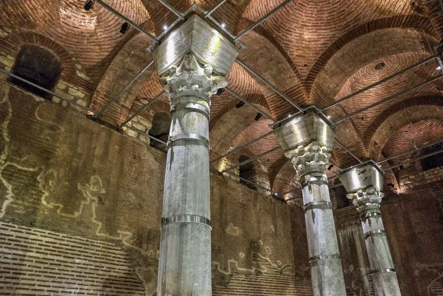 Illuminated marble columns and thick red brick vaults of the subterranean Theodosius Cistern in Istanbul, acting as a massive acoustic shield against the city above.