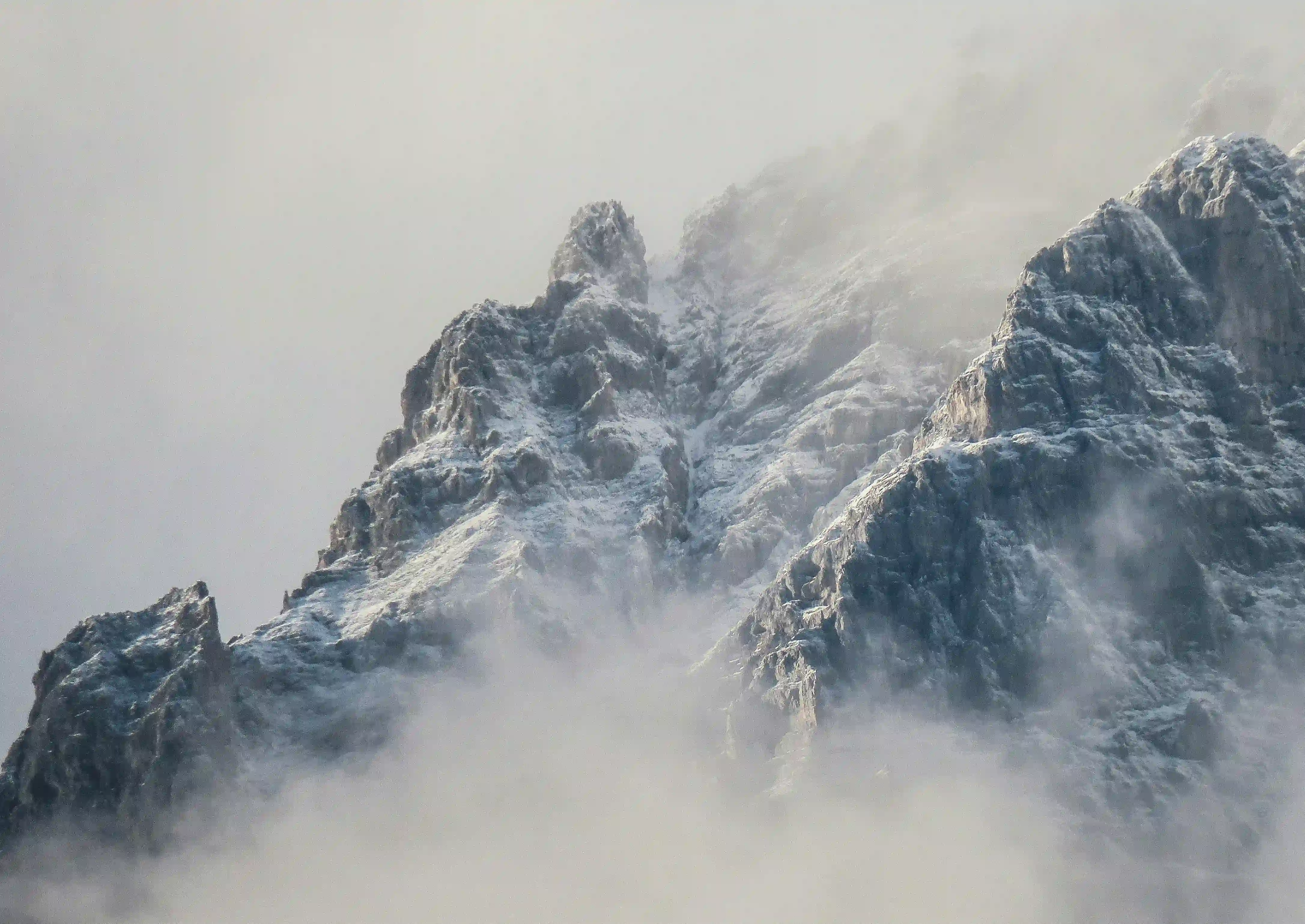 A rugged, snow-dusted mountain peak emerging from thick, freezing fog, representing extreme isolation and harsh nature.