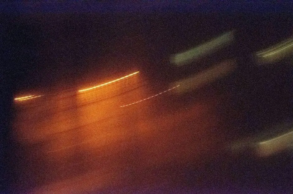 Abstract long exposure of warm light streaks cutting through a heavy grainy dark background.