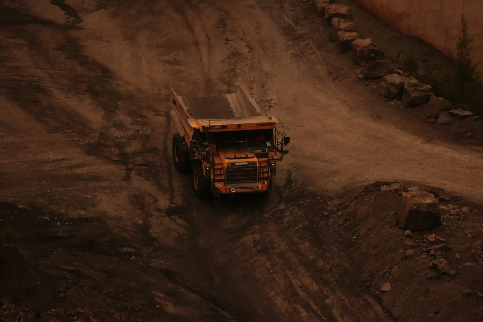 A massive yellow dump truck operating in a dark and dusty quarry representing the illegal sand mining industry.