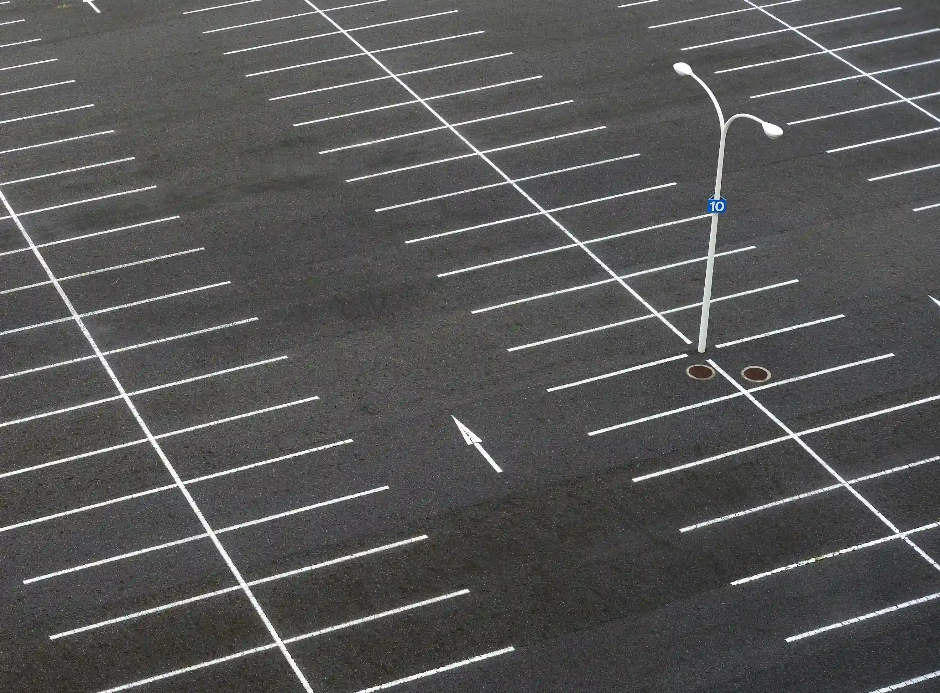 Minimalist aerial view of empty parking spaces with white lines on dark asphalt.