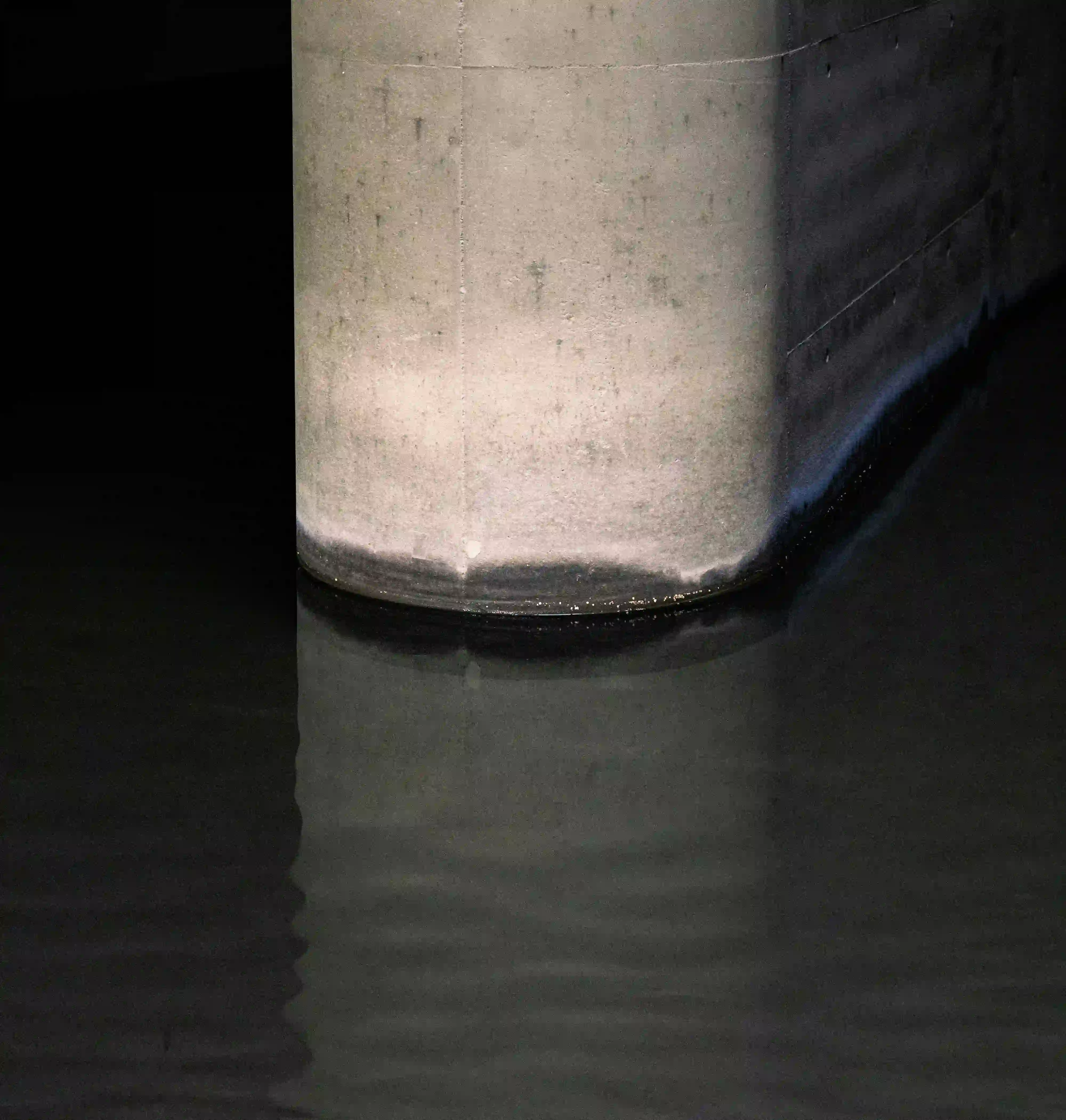 A massive concrete structure submerged in dark water, highlighting the brutalist engineering behind urban streams.