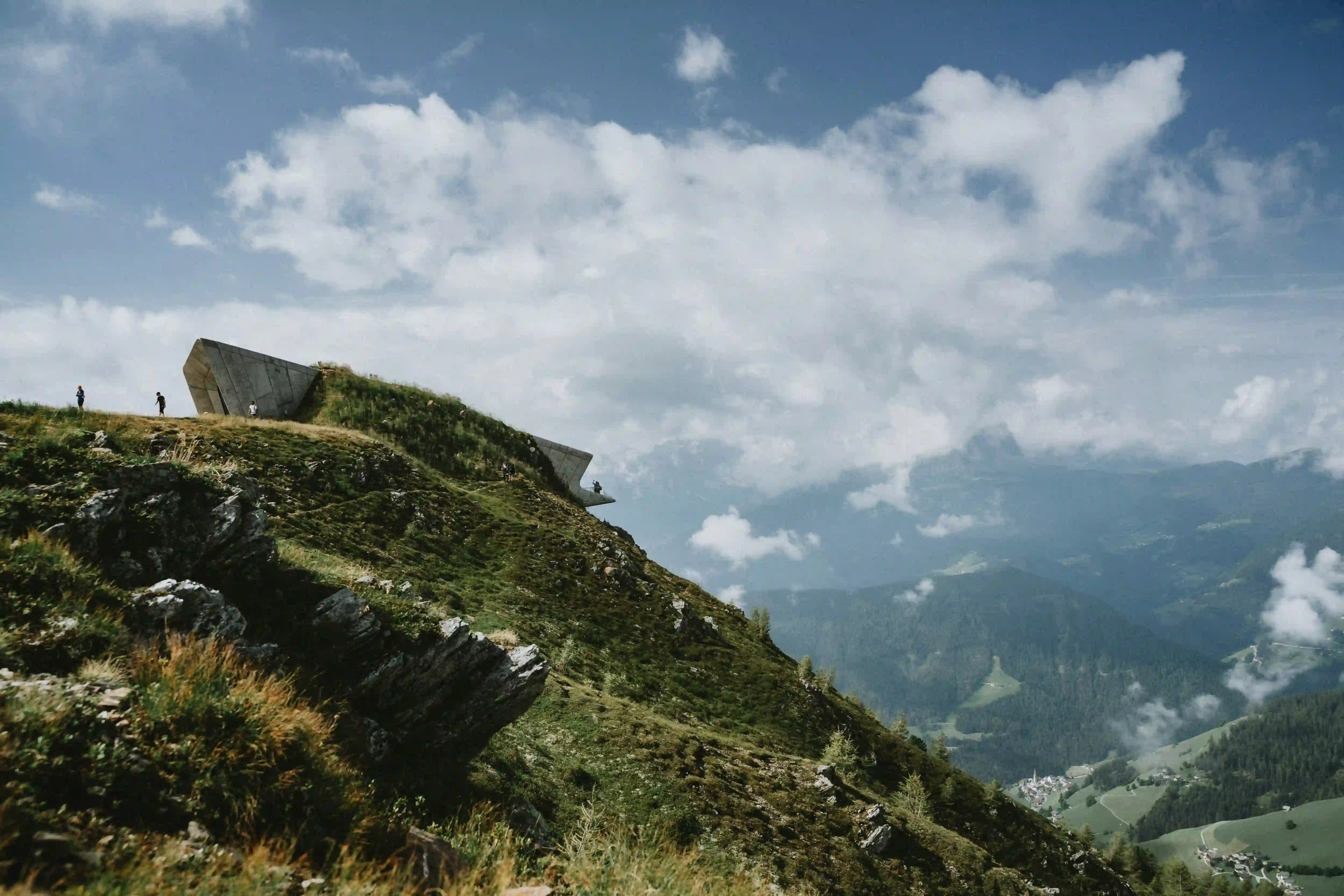 The concrete viewing platforms of the Messner Mountain Museum Corones emerging from the grassy rocky summit of Mount Kronplatz.