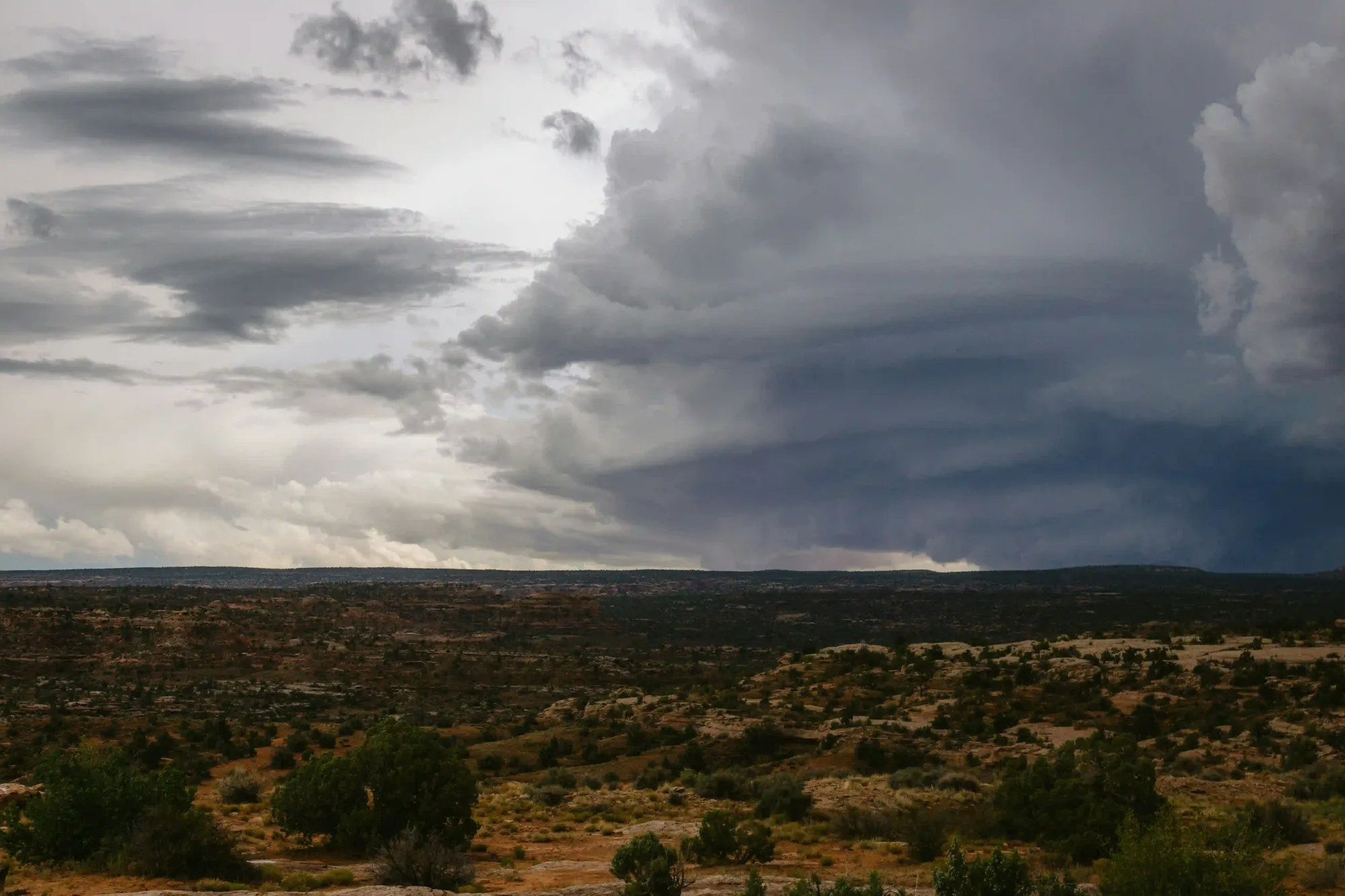 Heavy, dark storm clouds rolling over a vast, rugged landscape, symbolizing impending climate risks.