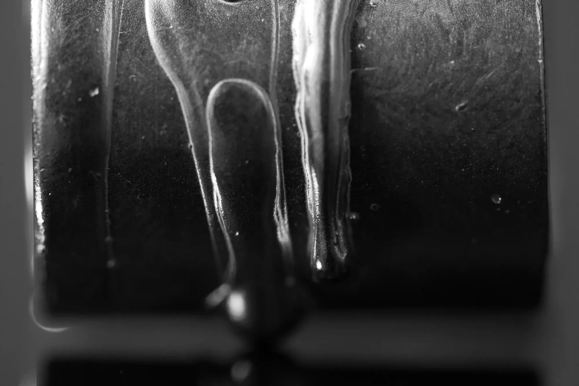 Close up macro shot of a dark viscous liquid dripping down a curved metallic surface.