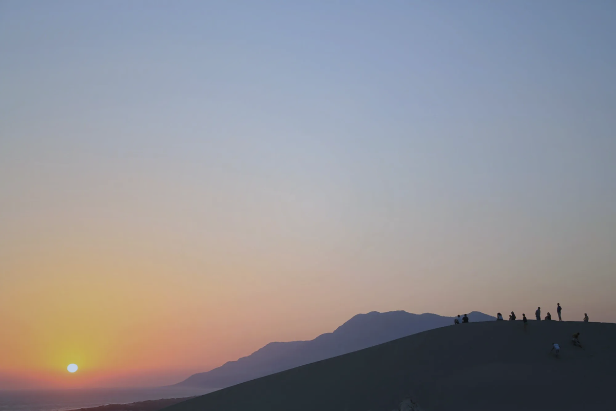 Silhouettes of people sitting on massive sand dunes watching the sunset at Patara, Turkey.